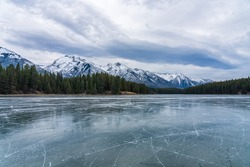 Johnson Lake frozen water surface in winter time. Snow-covered mountain in the background. Tourists here doing ice-skating in this season. Banff National Park, Canadian Rockies, Alberta, Canada.