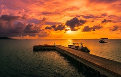 Wooden sea pier at sunset. Boat at sea pier at sunset. Orange sunset over sea pier. Pier boat at sunset sea