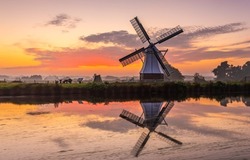 Mill by the river at dawn. Beautiful sunrise over windmill farm. Windmill at dawn. Windmill reflection in water at dawn