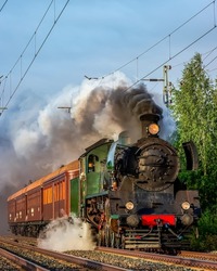Steam train rushes along the railway track. Vintage steam train. Steam train ride. Steam train