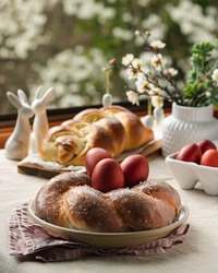 Easter traditional bread, austrian ostern zopf, greek tsoureki and red eggs on a table with linen tablecloth with spring window view, still life