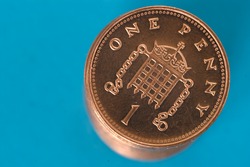 Stack of shiny new one penny coins, against a blue background