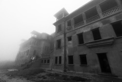 Dark mystic atmosphere of abandoned Bokor Palace Hotel in foggy. A group of tourists walks through the main entrance to Bokor casino hotel. Borkor Mountain, Kampot, Cambodia. Monochrome. Soft focus.