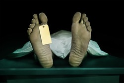Male human body lying dead at morgue with blank identity label and covered with sheet . Close-up foot of man cadaver with identification toe tag in human life loss and death concept isolated on black