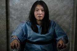 young crazy and mentally insane Asian woman restrained in wheelchair at mental hospital suffering psychiatric disorder as schizophrenia looking catatonic in Korean horror movie style