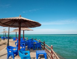 Beach cafe with plastic furniture, tables, chairs, wooden parasols in resort city. Clear sunny day. Beautiful outdoor fenced place on sea bank to eat and relax. Picturesque seascape, marine view