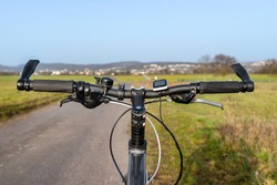 A bicycle handlebar seen from the first person perspective. Visible bicycle frame and bicycle accessories on the handlebar, and the road in the background.
