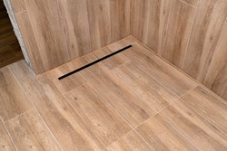 Modern black linear drain in a bathroom lined with ceramic tiles imitating wood.