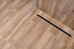 Modern black linear drain in a bathroom lined with ceramic tiles imitating wood.