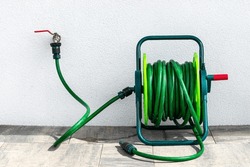 A garden hose connected to a faucet protruding from a building against a white facade.