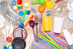 Disposable single use plastic objects such as bottles, cups, forks, spoons and drinking straws that cause pollution of the environment, especially oceans. Top view on sand