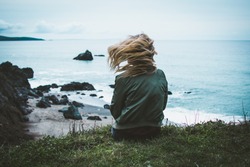 girl sitting on a cliff overlooking the ocean with her hair blowing