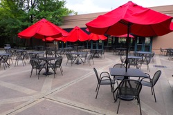 Red umbrella with black chairs and tables in outdoor public park restaurant.