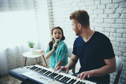 Single father plays on synthesizer while daughter sings song into microphone. Accompaniment. Fatherhood.