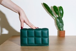 female hand on a small bag made of green eco-leather and a cactus in a flower pot