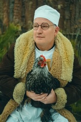 Portrait man doctor veterinarian holds a rooster in his hands on the street in winter at the ranch
