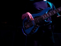 Hand playing solo bass guitar on stage on dark background with copy space. Musician, bass guitarist performance in rock band concert.
