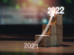 Shining rise up arrow on wooden blocks chart steps with percentage icons from year 2021 to 2022 on wooden desk, business growth process, and economic improvement concept.