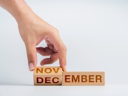 Changing to the last month of the year. The hand is flipping wooden cube blocks for change words, months from November to December on the desk on white background, clean, modern, and minimal style.