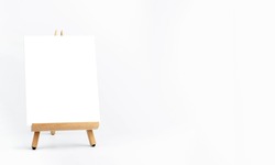 White blank artist frame on a small wooden easel on white background with copy space. Advertising mockup artboard for pictures or artwork. Painting frame template on easel stands display banner.