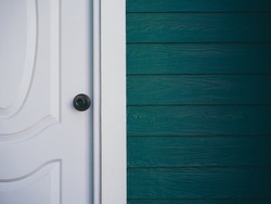 Close up the white vintage clean front door with iron knob near wood plank wall, dark green color with copy space.