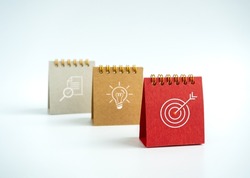 Business action plan with goal,  idea and research icon signs on small red, beige and grey desk calendar year 2023 on white background. Three step of strategy concept, minimal style.