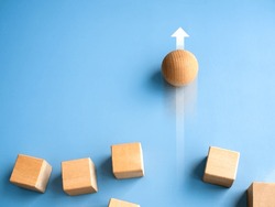 Leadership, business success, unique, difference, challenge, and motivation concepts. Wooden sphere rolling fastest, leading with rising arrow and following with wood cube blocks on blue background.