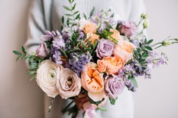 Very nice young woman holding big and beautiful colourful flower wedding bouquet with purple carnations and mattiolas, cream David Austin roses, ranunculus and pistachios