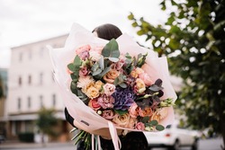 Very nice young woman holding big and beautiful bouquet of fresh roses, eustoma, eucalyptus, carnations
hydrangea flowers in cream and purple colors, cropped photo, bouquet close up