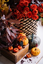 Beautiful red, yellow and orange coloured flowers standing on the table with tiny decorative oriental pumpkins, making autumn outlay, vertical photo