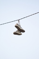 Old sneakers hang on wires against the sky.