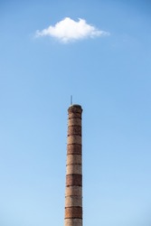 A tall brick chimney against a blue sky with a white cloud.