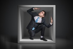 Young businessman trapped inside uncomfortable small box.