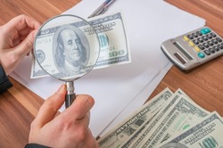 Viewing fake or counterfeit dollar banknote with magnifying glass.