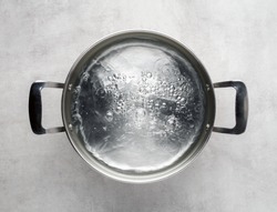 Stainless steel metal cooking pot of boiling water on gray concrete background , top view. 