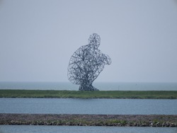 Antony Gormley's statue of a man sitting on his heels on an enclosure dam in Lelystad, Netherlands