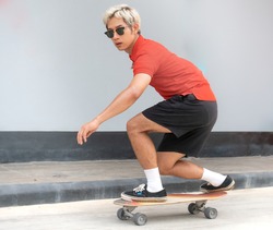 Young asian man riding skateboard on a city street. Portrait of male in t-shirt and black short pants exercise surf skate near sidewalk in urban. Trendy outdoor extreme sport recreation in Asia. 