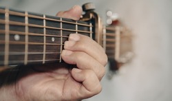 Older woman musician hand holds the neck of classic wooden guitar play A chord sound B key as capo fret two. Senior guitarist put fingers on fingerboard playing chord A song. String musical instrument