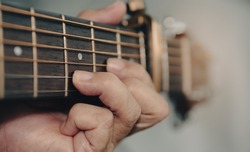 Senior woman musician hand holds the neck of classic wooden guitar play D chord sound E key tone as capo fret two. Guitarist put fingers on fingerboard playing guitar. Selective focus blur background.