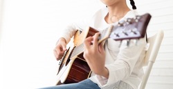 Young girl musician holds wooden acoustic guitar neck and fingerpicking melody. Female kid guitarist put fingers on fingerboard playing guitar. String musical instrument. Selective focus right hand.