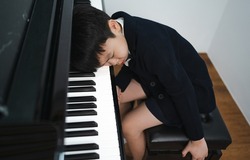 Adorable lazy little boy in black suit sits at grand piano sleep. Cute boring kid pianist feels tired to practice playing classic songs keyboard. Playful child musician refuses to perform concert