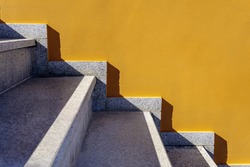 Side view on bright yellow or mustard painted wall and white marble stairs. Geometrical pattern, straight lines, light and shadow contrast. Graphic art, modern design, urban architecture. Copy space.