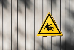Yellow triangular road sign warning for risk of falling hanging on the gray fence. triangular traffic sign warning for danger of falling or steep grade. Yellow falling man -Warning hazard sign