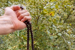 male monk holds in his fist the beads used for keeping count during meditations and concentrations, close-up, selective focus. A string of wooden rosary beads for prayer and meditation in a hand