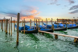 Gondolas line up at the pier along the grand canal as the sun sets in Venice, Italy