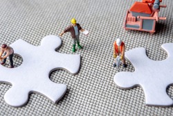 solving problems fiting together of empty puzzle pieces, miniture figurines working on white puzzle pieces, may be used in corporate topics