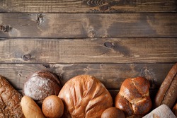 Variety of baked goods on wooden table background. Bakery concept - gold rustic crusty loaves of bread and buns. Still life captured from above (top view, flat lay), banner layout. Copy space