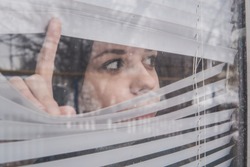 Woman Looking Through the Blinds. Girl looking out the window
