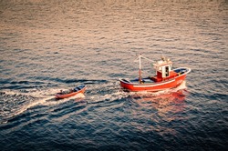 Small boat in the sunset. Red boat. Vintage color. Small ship towing another boat sailing out of a harbour. Tenerife, Canary Islands Spain