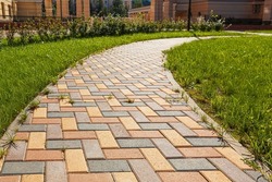 The pedestrian path is paved with multi-colored paving stones. Grass grows between the tiles. Selective focusing.
